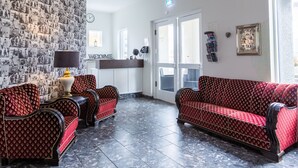 A lobby with patterned red sofas, a reception desk, a wall clock, and a 'Welcome' sign. - Guesthouse Hamar (Vestmannaeyjar)