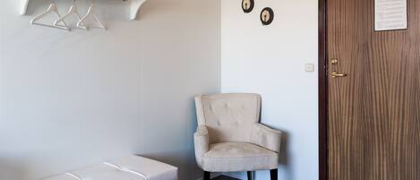 Una habitación con un banco, una silla, una puerta de madera y un perchero de pared.
