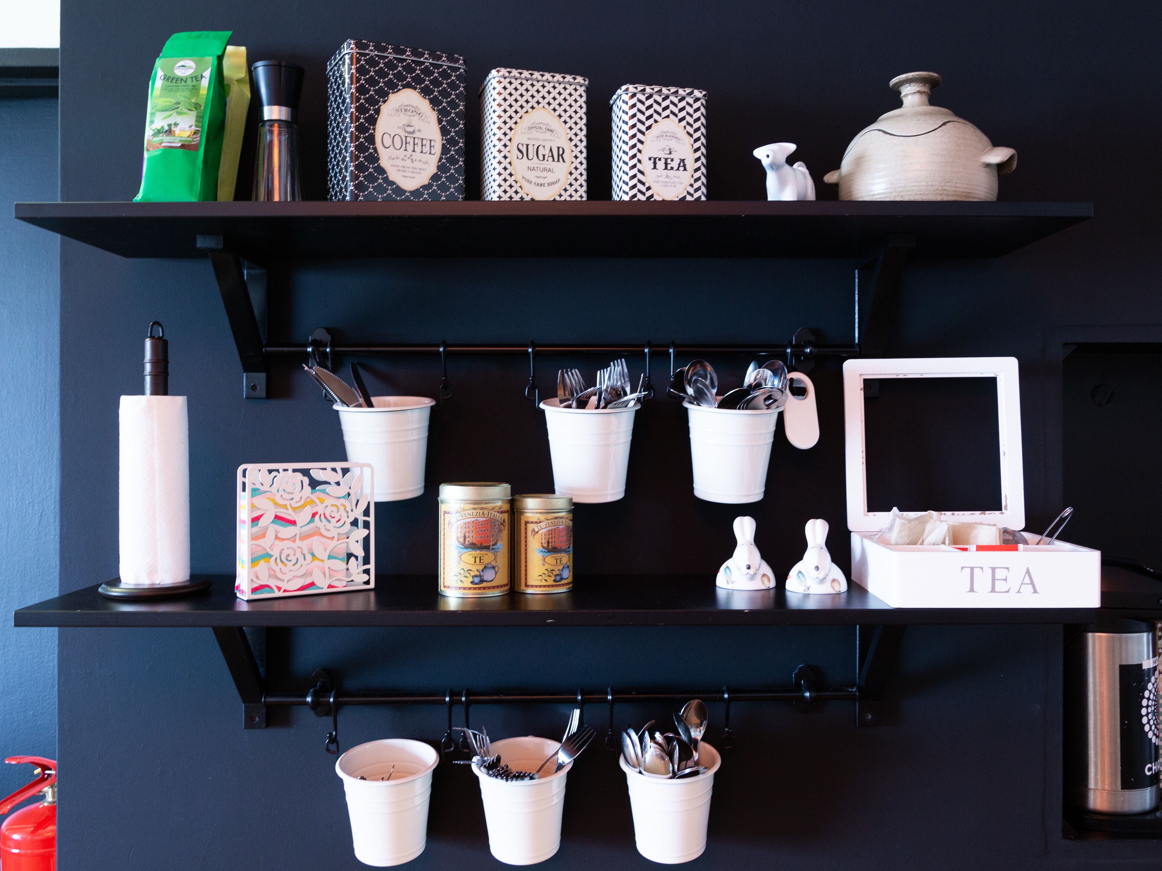 Uma prateleira na cozinha com chá, café, açúcar e um bule.