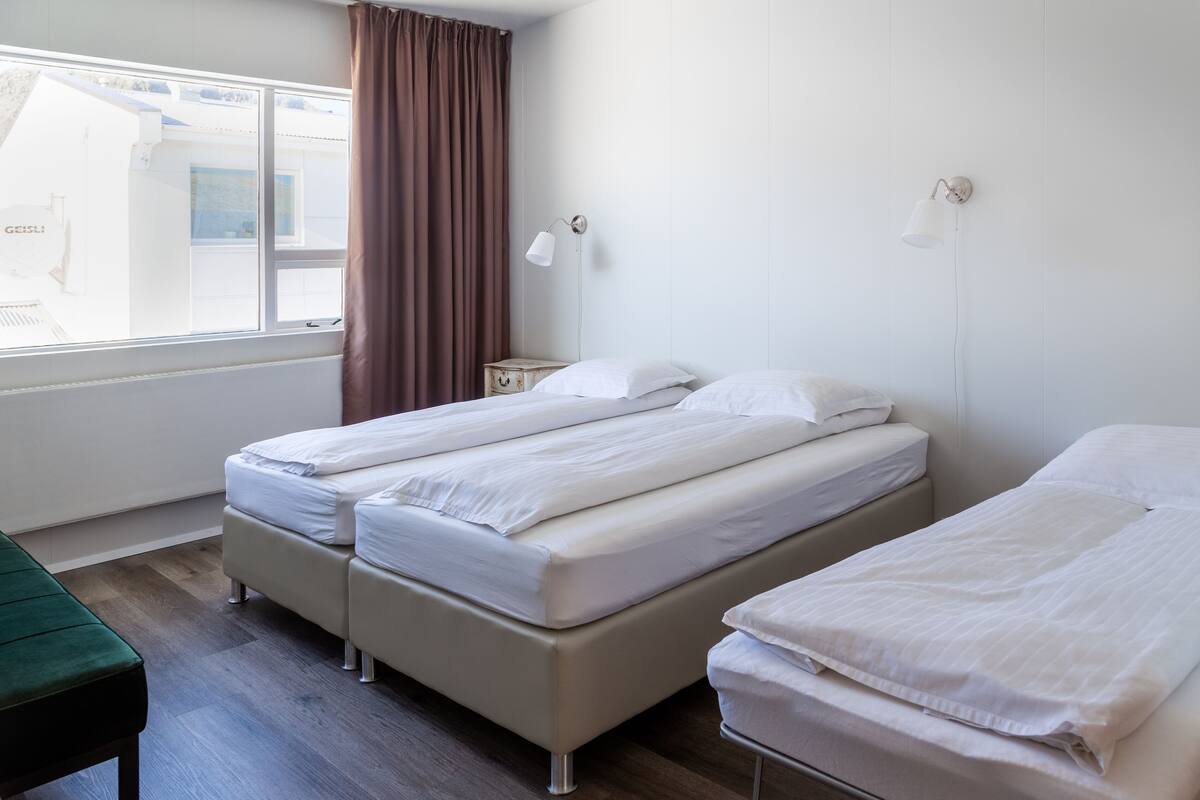 Une chambre avec deux lits, une fenêtre avec des rideaux et une table de chevet avec une lampe.
