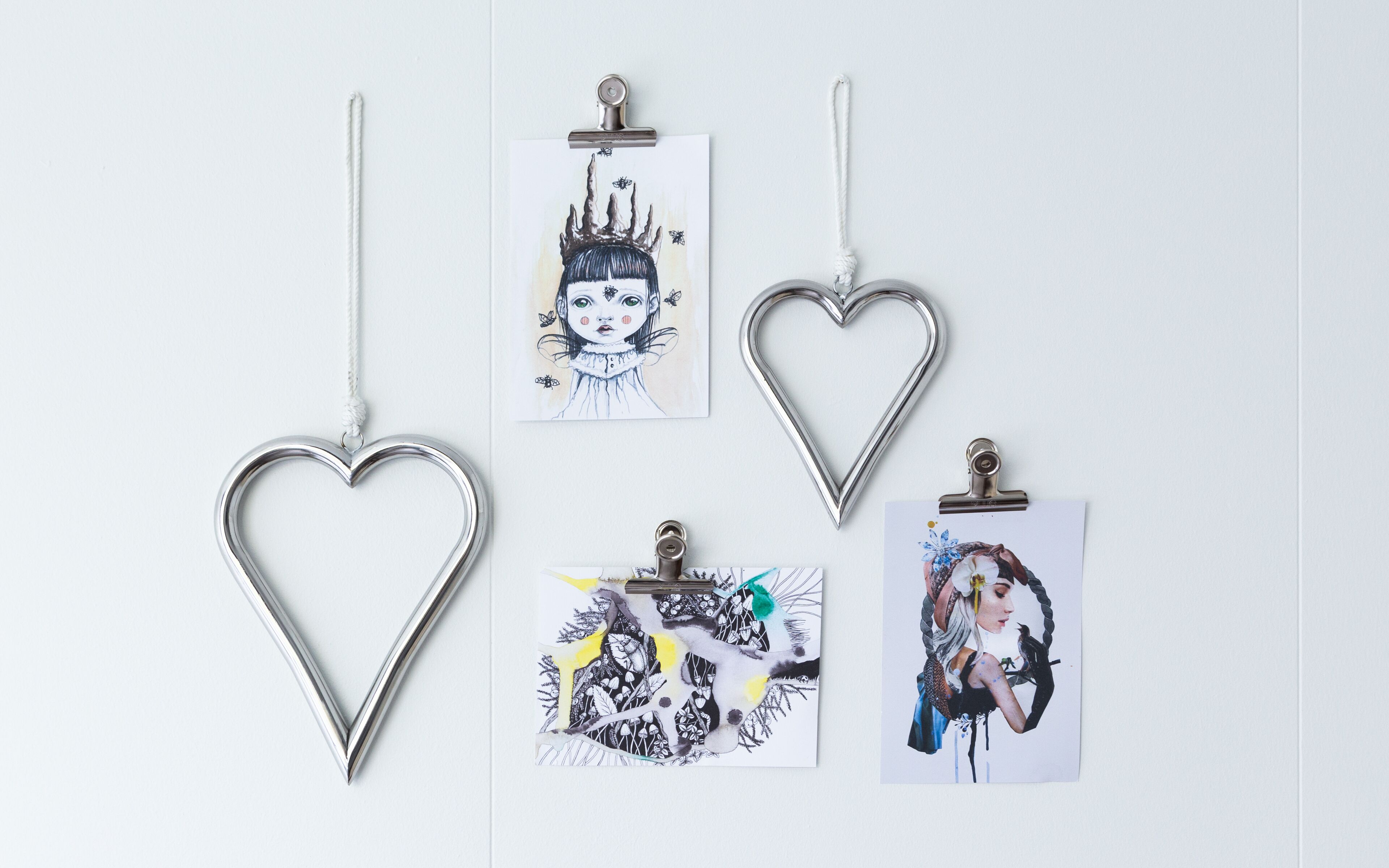 A wall with four artworks, each clipped to the wall with a metal hanger.