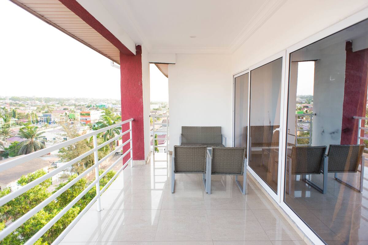 A balcony with two wicker chairs, a glass door, and a view of a cityscape.