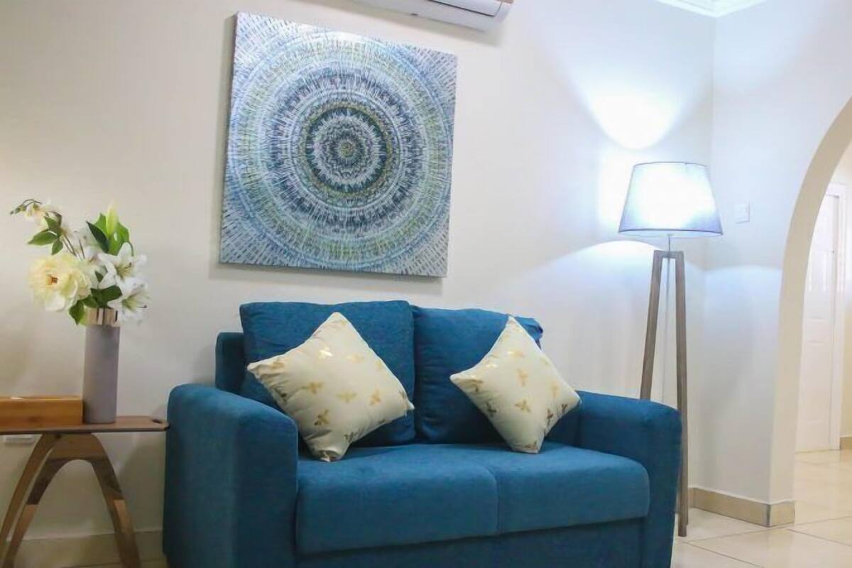 A blue sofa with two pillows, a wall art piece, a floor lamp, and a vase with flowers.