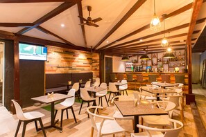 Restaurante com várias mesas e cadeiras, área de bar e uma televisão fixada na parede.
