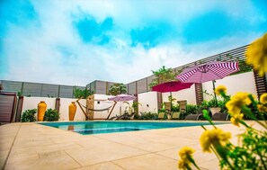 A swimming pool with lounge chairs and umbrellas, surrounded by a fence and plants. - Earl Heights Suites Hotel (Accra)