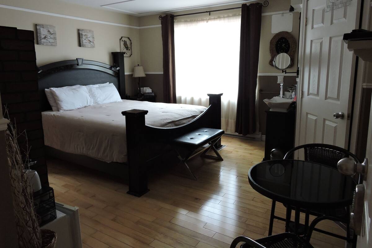 Un dormitorio con cama, mesita de noche, lámpara y una pequeña mesa con sillas.