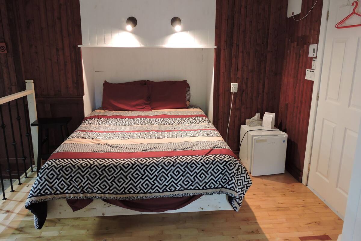 Una cama con ropa de cama estampada, una mesita de noche con lámpara y un calentador fijado a la pared.