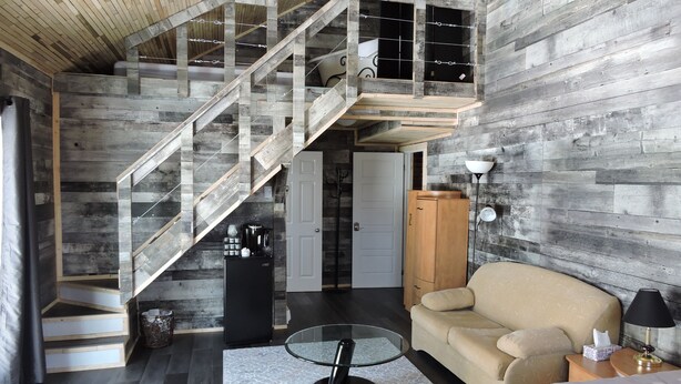 Un espacio habitable tipo loft con una escalera de madera, un sofá, una mesa de centro y un armario.