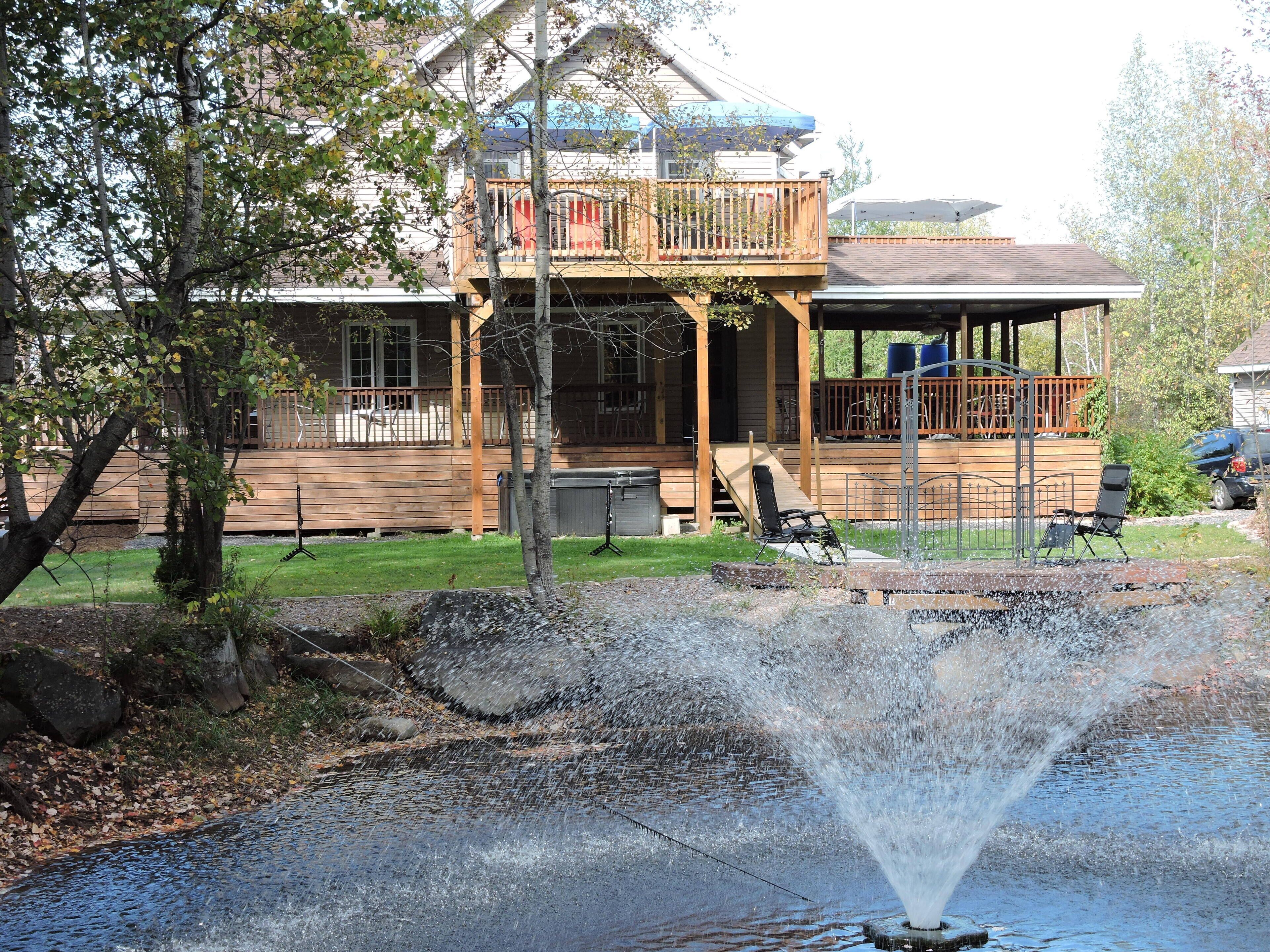 Une maison avec une terrasse en bois, un porche couvert et une fontaine dans le jardin.