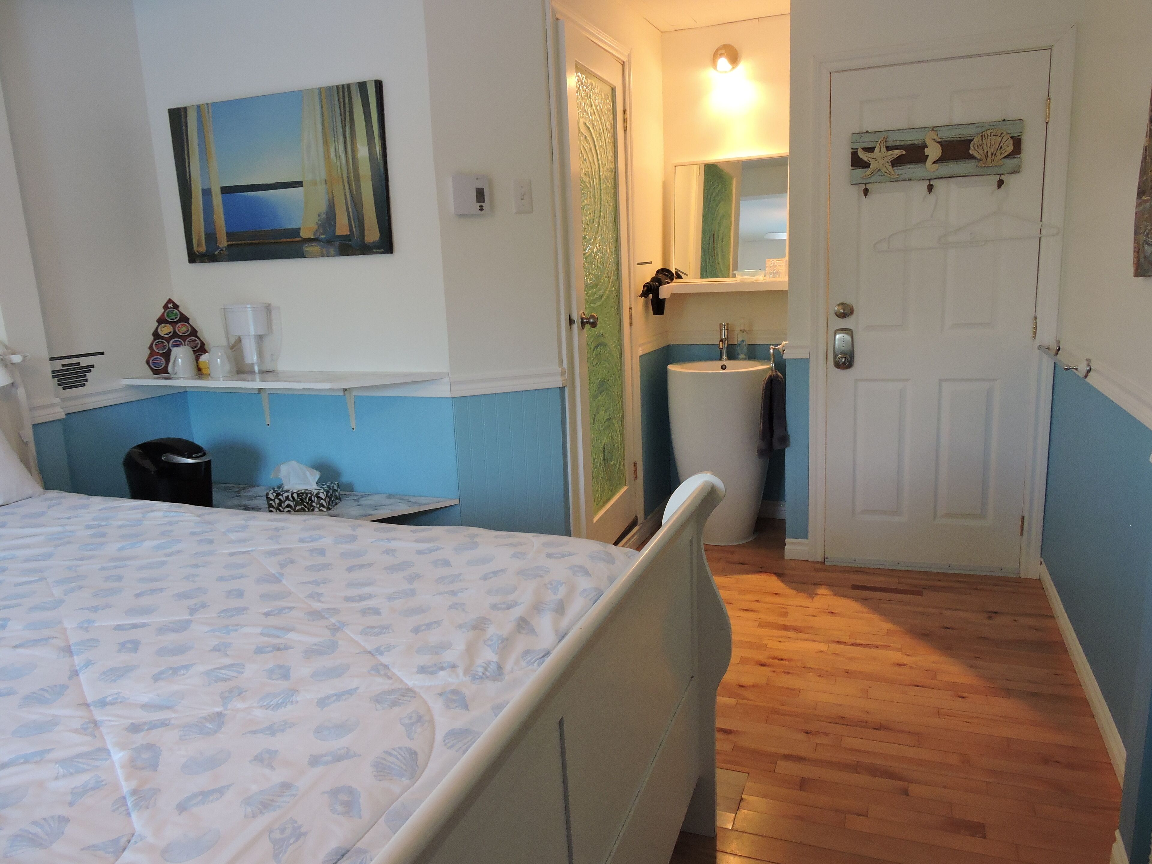 A bedroom with a bed, a painting, a sink, and a door.