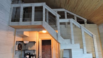 A wooden staircase with a brick wall at the bottom, leading to a loft area with a white railing and a fan.