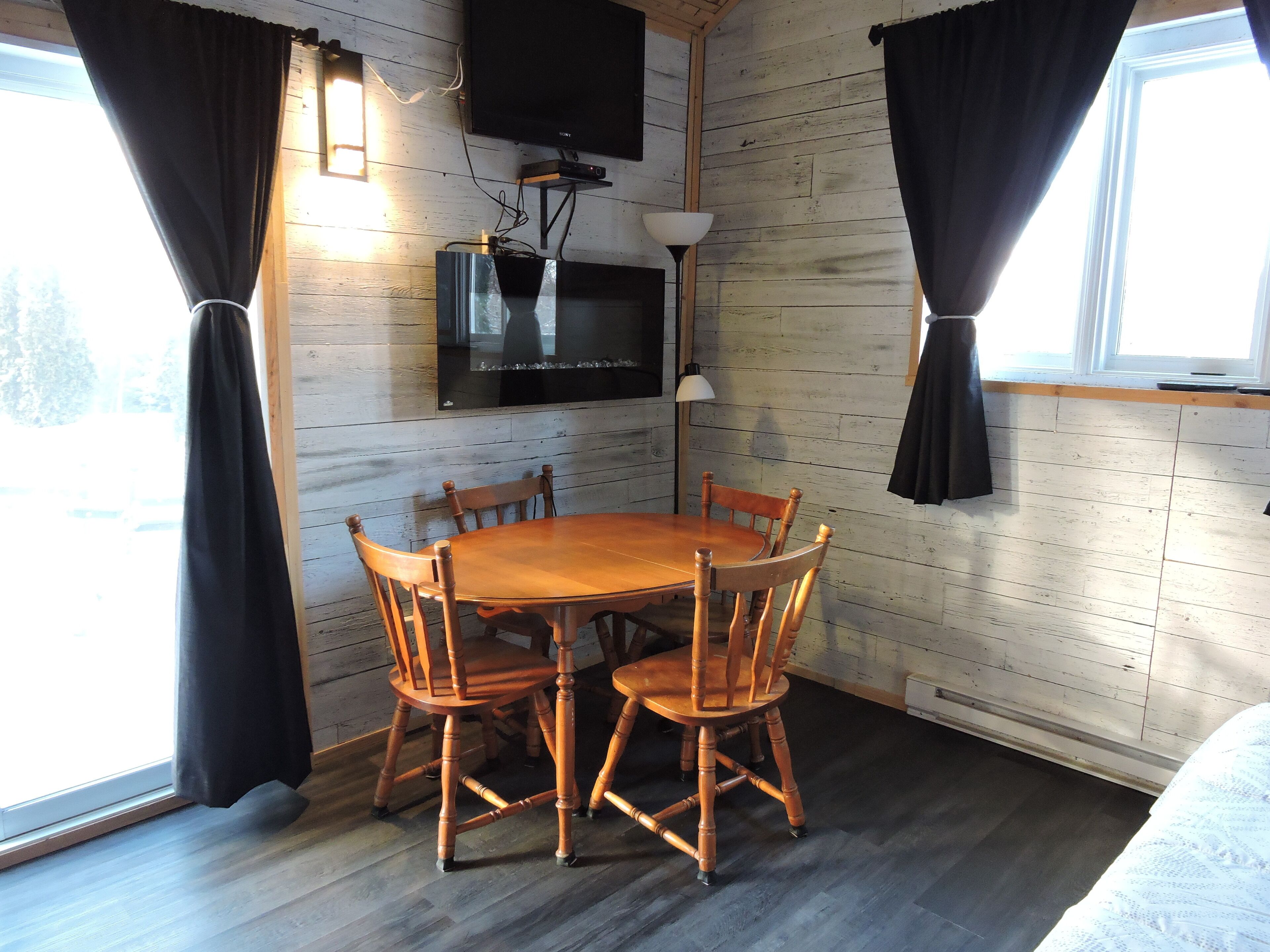 A cozy room with a wooden dining table and chairs, a flat-screen TV mounted on the wall, and a window with curtains.