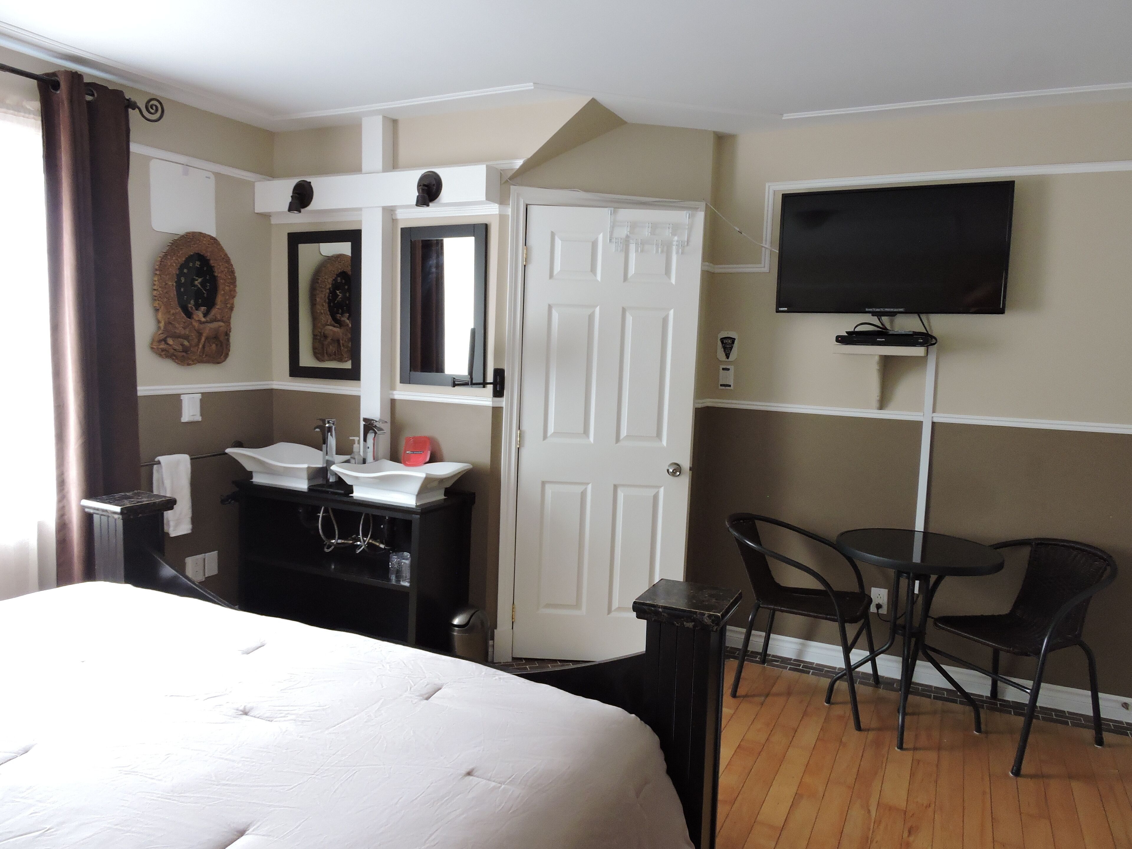 Een hotelkamer met een bed, een badkamer met een wastafel en spiegel, een aan de muur bevestigde televisie, en twee stoelen.