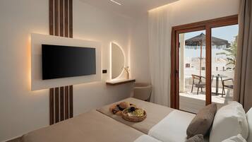 Una habitación de hotel moderna con una televisión de pantalla plana montada en la pared, una cama cómoda con vista al área de estar exterior, y un balcón con una mesa y sillas.