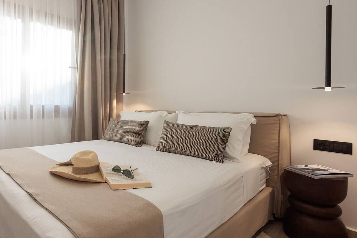 Un lit bien fait, recouvert d’une couverture beige, avec un chapeau et des lunettes de soleil posés dessus.