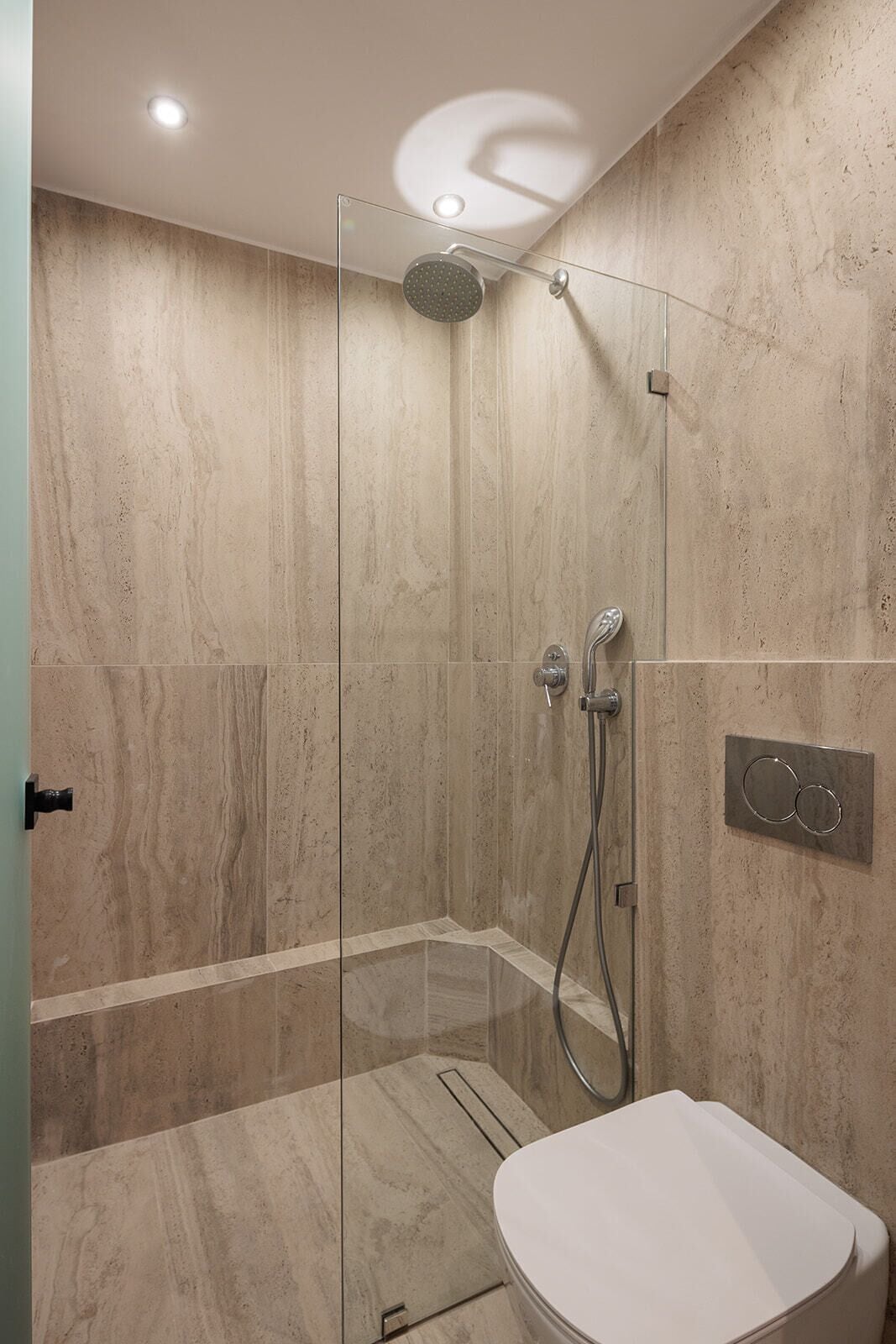 A modern bathroom with a glass-enclosed shower, a toilet, and a wall-mounted control panel.