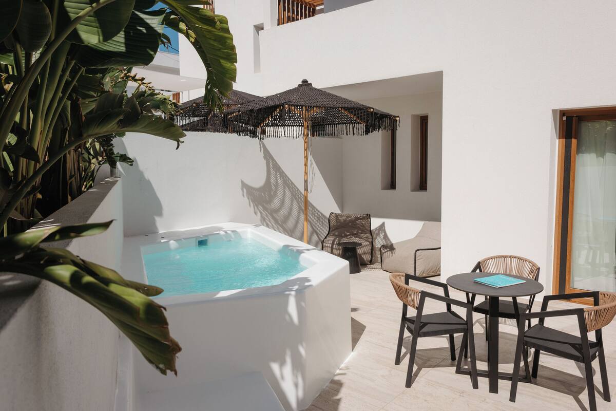Un espace extérieur moderne doté d’un jacuzzi, de meubles en osier et d’un grand parasol.