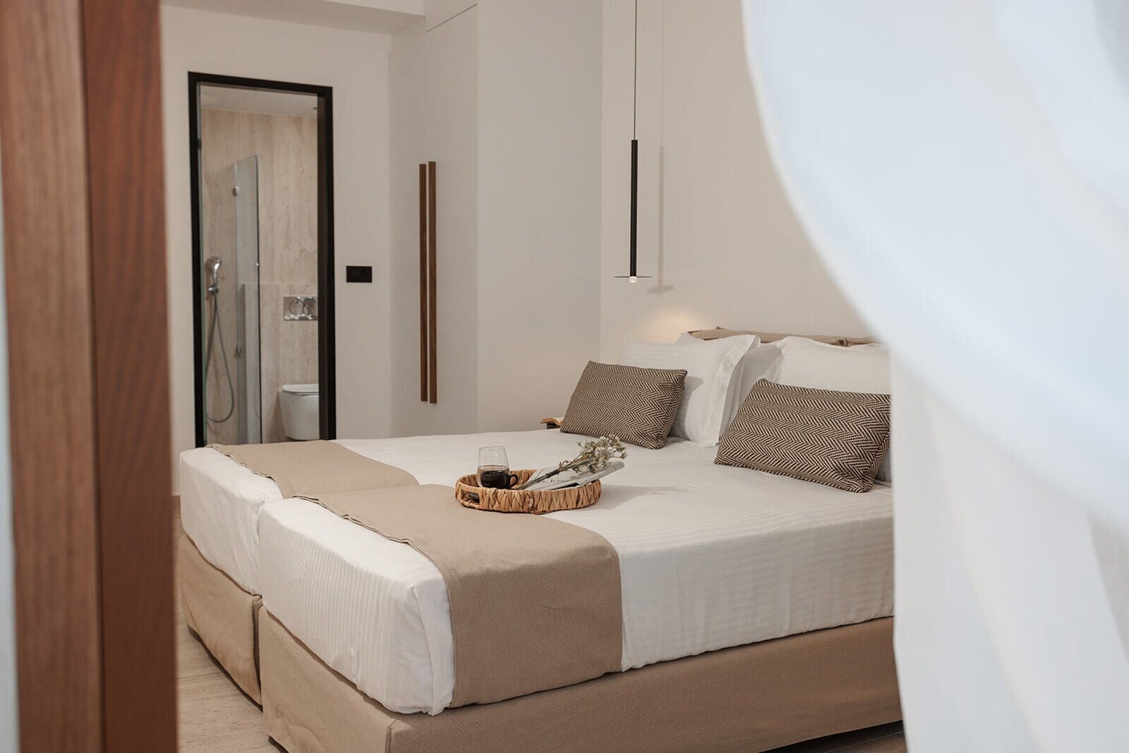 A modern bedroom with a large bed, a bedside table with a tray, and a shower area visible through an open door.