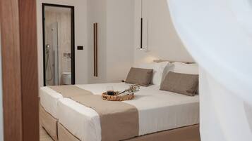 A modern bedroom with a large bed, a bedside table with a tray, and a shower area visible through an open door.