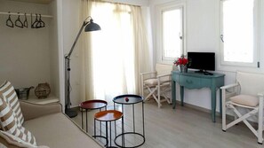 Ein Wohnzimmer mit einer Couch, zwei kleinen Tischen, einem Fernseher auf einer türkisblauen Kommode und einer Stehlampe.