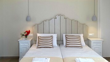 A double bed with striped pillows, a nightstand with a vase of flowers, and a wall-mounted light fixture.