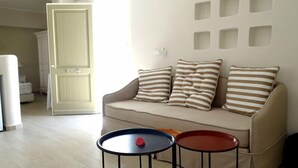 Un salon avec un canapé beige, des coussins à rayures et deux petites tables rondes.
