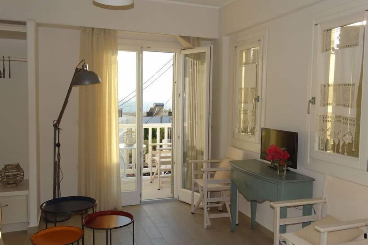 Une chambre avec un balcon, un bureau agrémenté d’un vase de fleurs et une chaise.
