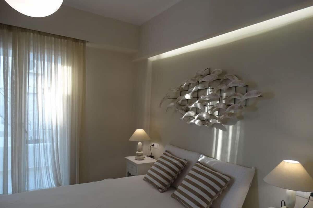 Une chambre d’hôtel avec un grand lit, deux tables de chevet avec des lampes, un élément décoratif mural et des rideaux légers.