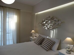 A hotel room with a large bed, two bedside tables with lamps, a decorative wall piece, and sheer curtains. - Naxos Oceamo (Naxos)