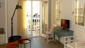 Une chambre avec un balcon, un bureau agrémenté d’un vase de fleurs et une télévision.