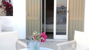 A patio area with white furniture, a metal bucket with flowers, and a sliding glass door leading to a balcony. - Naxos Oceamo (Naxos)