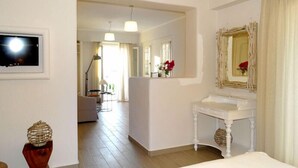 Une chambre d’hôtel avec une coiffeuse blanche, un grand miroir et un plancher en bois. Un couloir mène à un coin repas équipé d’une table et de chaises.