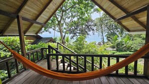 Een houten terras met een hangmat, houten leuningen en uitzicht op de oceaan en groen.