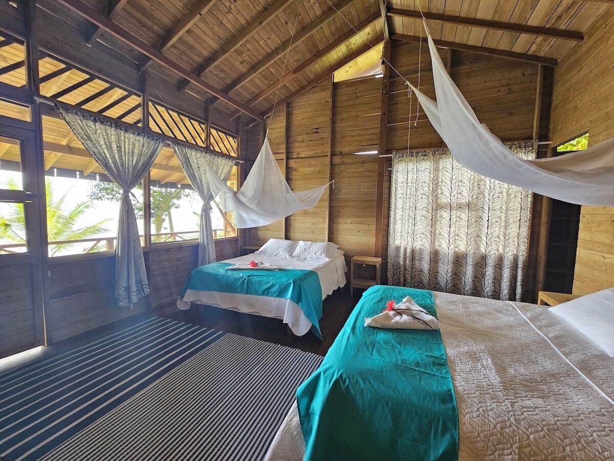 A room with two beds, a wooden ceiling, and a view of palm trees.