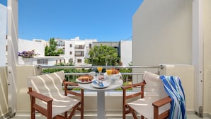 A balcony with two wooden chairs, a table with breakfast items, and a view of buildings in the background. - Ormos Holiday Studios (Naxos)