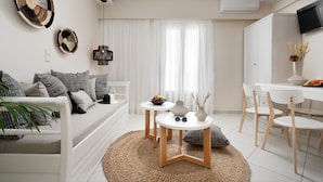 A modern living room with a sofa, two side tables, a dining area with chairs, and a TV mounted on the wall. - Ormos Holiday Studios (Naxos)