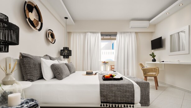 A modern hotel room with a large bed, a desk, and a TV. - Ormos Holiday Studios (Naxos)