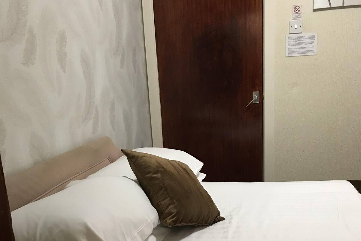 Ett hotellrum med en säng, en trädörr och en vägg med en ljusströmbrytare och en skylt som förbjuder rökning.