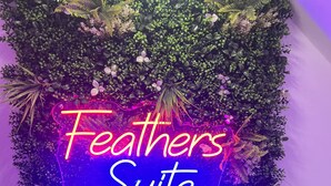 A neon sign with "Feathers Suite" and an arrow pointing right, surrounded by lush green foliage. - The Feathers Hotel (Blackpool)