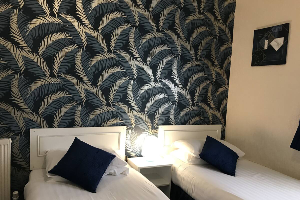 Ett hotellrum med två separata sängar, vitt sänglinne och en mörk tapet med ett bladmotiv.