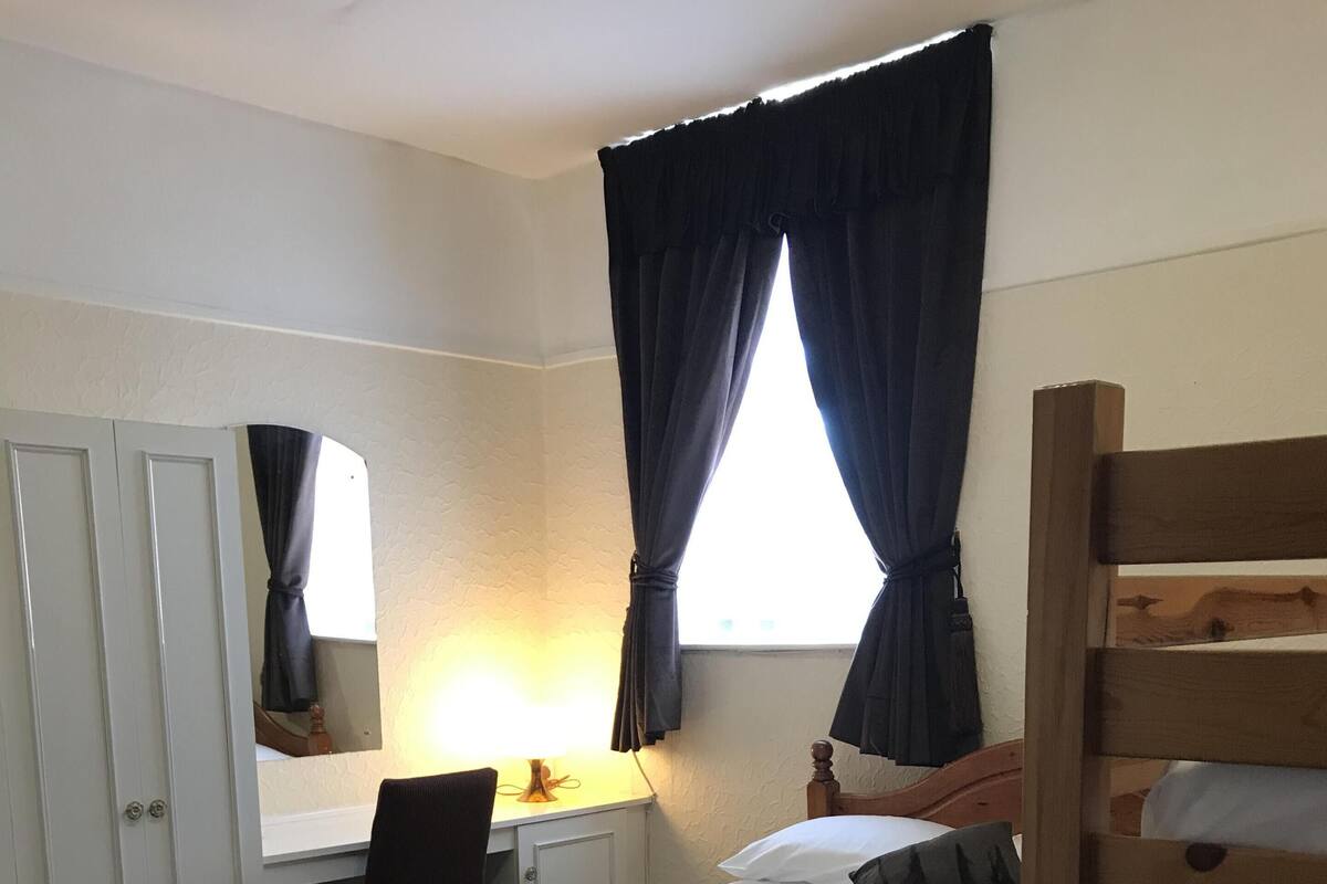 Ett hotellrum med en säng, ett skrivbord, en stol, en garderob och ett fönster med gardiner.