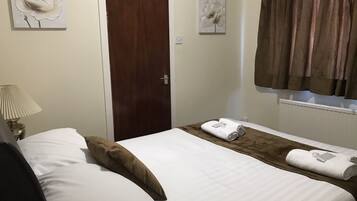 A hotel room with a bed, a nightstand with a lamp, a wooden door, and two wall-mounted flower paintings.
