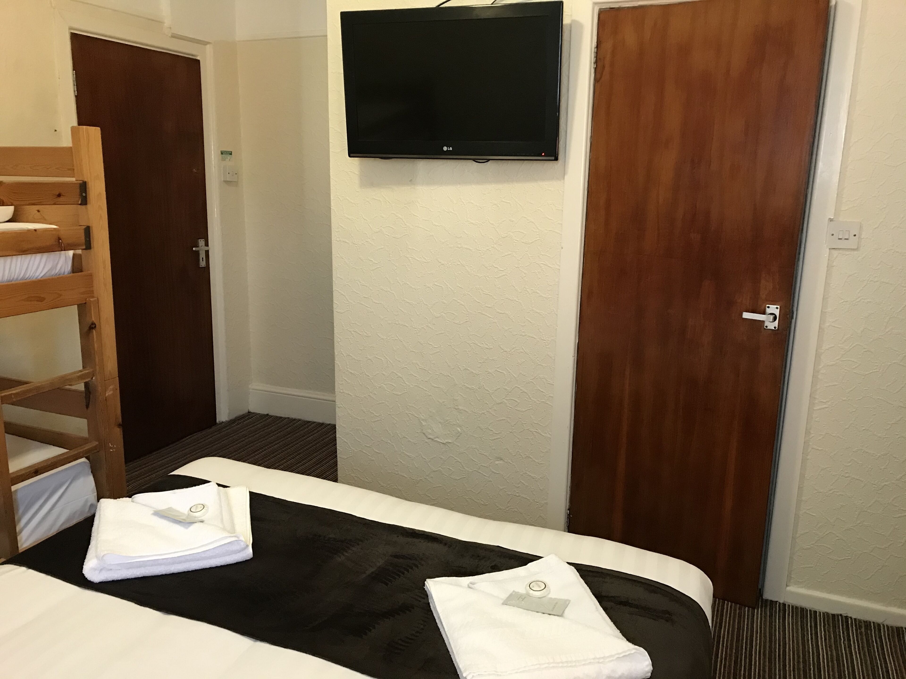 A hotel room with a bed, a TV mounted on the wall, and two wooden doors.
