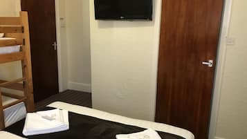 A hotel room with a bed, a TV mounted on the wall, and two wooden doors.