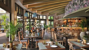 En restaurant med flere borde og stole, et barområde, og store vinduer som giver naturligt lys.