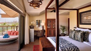 A bedroom with a four-poster bed, a desk with a chair, a small seating area with cushions, and a view of the outdoors. - Lapita, Dubai Parks and Resorts, Autograph Collection (Dubai)