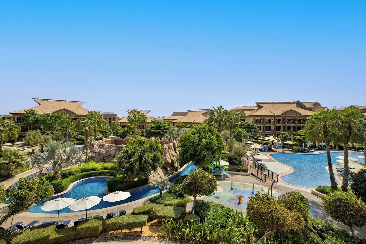 A resort with multiple swimming pools, palm trees, and a large building in the background.