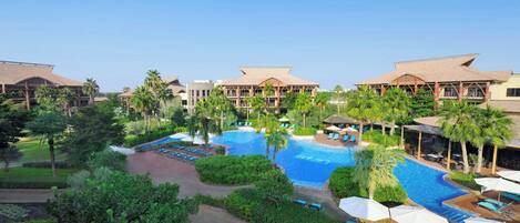 Een resort met meerdere zwembaden, palmbomen en een fraai onderhouden tuin.