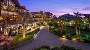 A multi-story hotel with outdoor dining areas, palm trees, and a well-lit pathway. - Lapita, Dubai Parks and Resorts, Autograph Collection (Dubai)