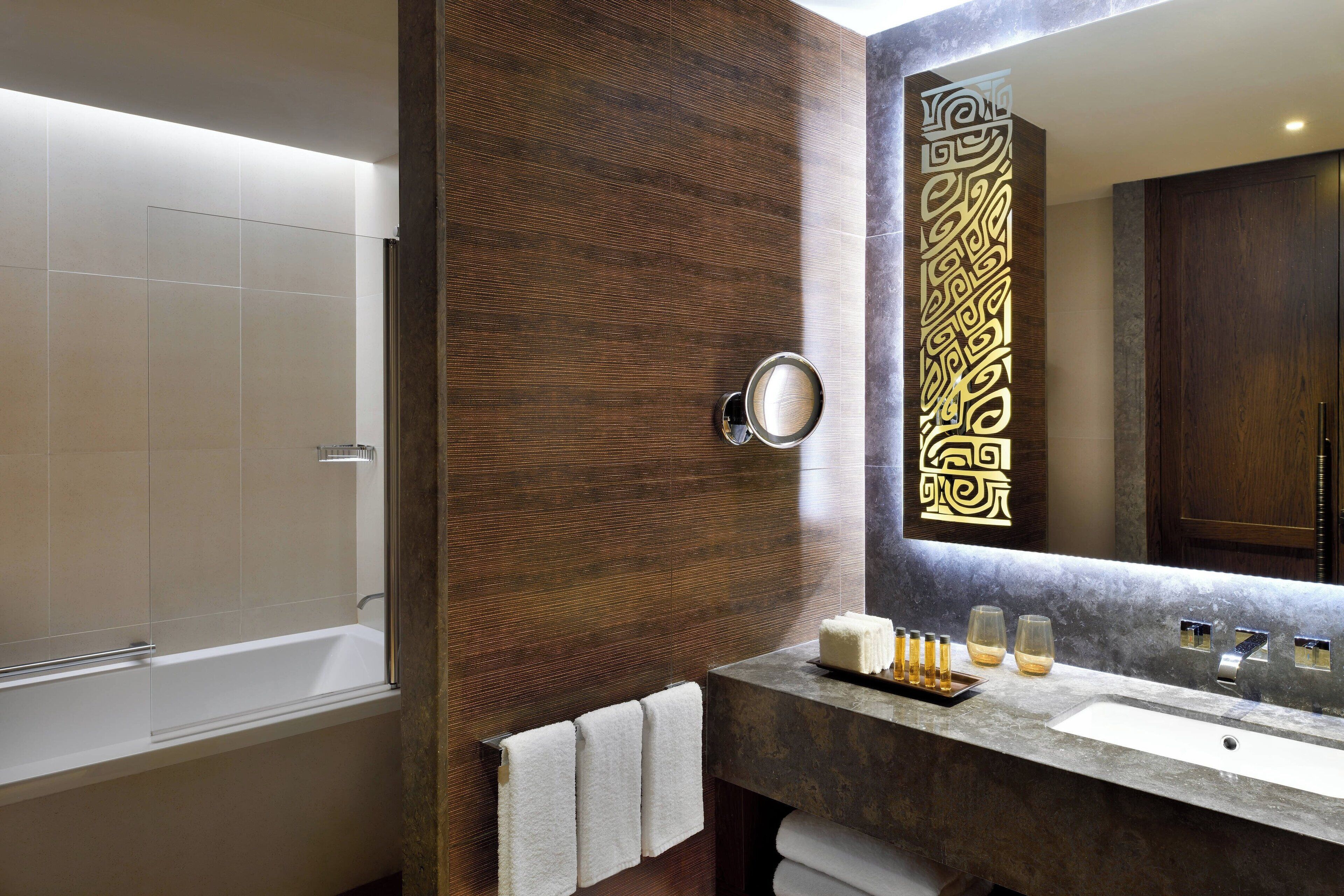 A modern bathroom with a wooden vanity, a large mirror, and a bathtub.